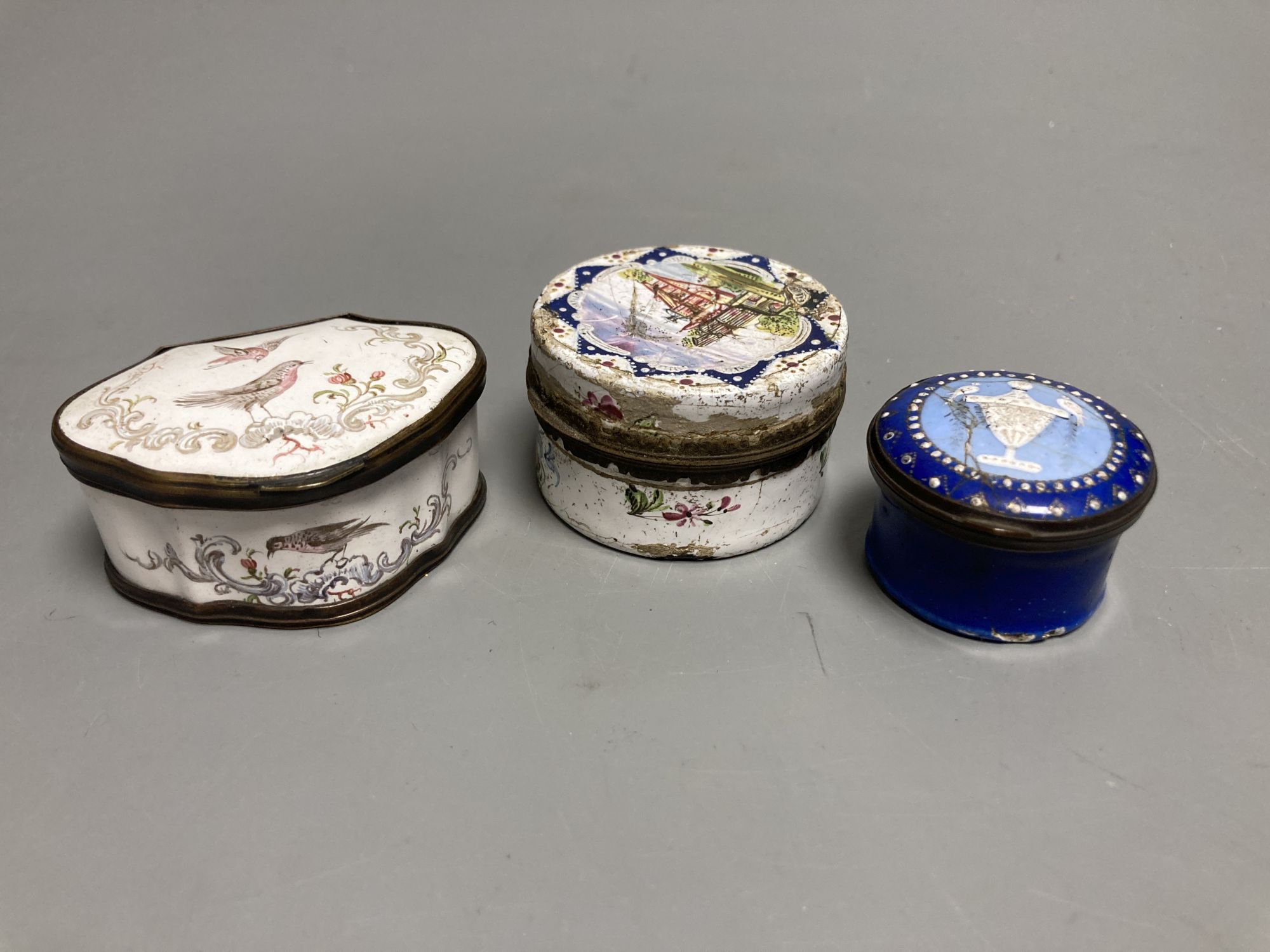 An 18th century white enamelled box painted with a palace, 5cm., a cartouche shaped box decorated with a birds, 6cm. and a patch box de